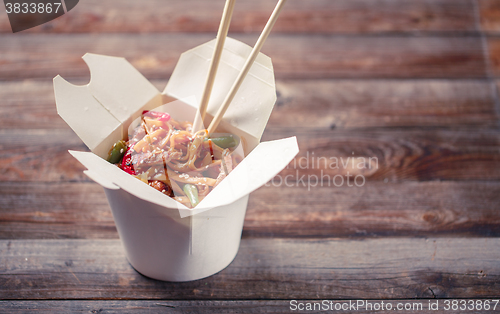 Image of Noodles with pork and vegetables in take-out box on wooden table