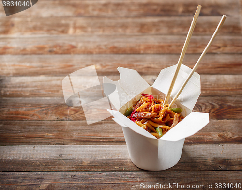 Image of Noodles with pork and vegetables in take-out box on wooden table