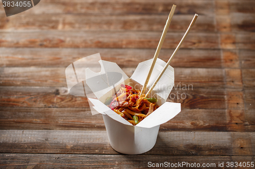 Image of Noodles with pork and vegetables in take-out box on wooden table