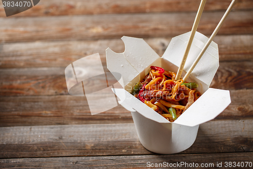 Image of Noodles with pork and vegetables in take-out box on wooden table