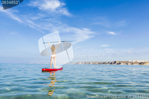 Image of A beautiful and happy woman with arms up and learning paddle-sur