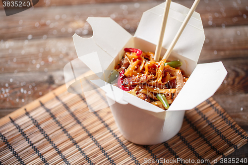 Image of Noodles with pork and vegetables in take-out box on wooden table