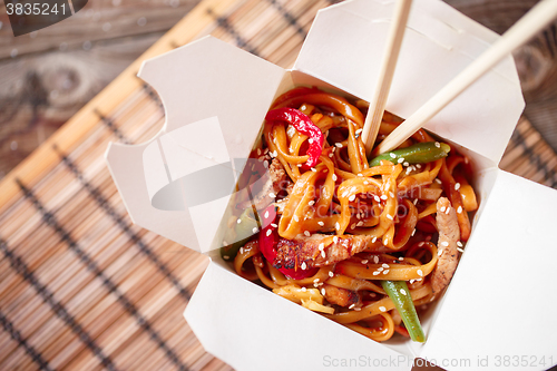 Image of Noodles with pork and vegetables in take-out box on wooden table