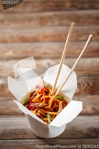 Image of Noodles with pork and vegetables in take-out box on wooden table