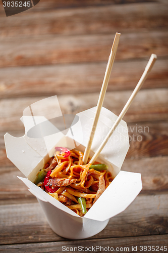 Image of Noodles with pork and vegetables in take-out box on wooden table