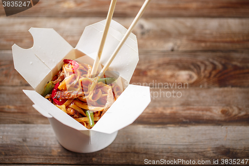 Image of Noodles with pork and vegetables in take-out box on wooden table