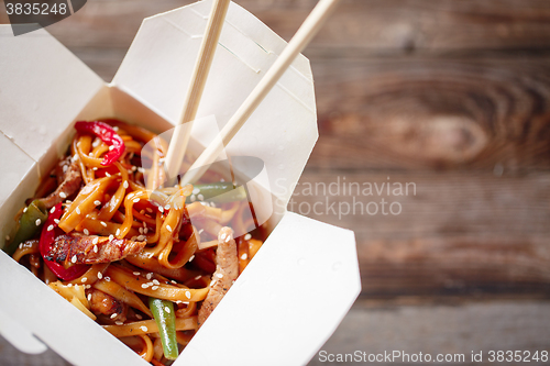 Image of Noodles with pork and vegetables in take-out box on wooden table