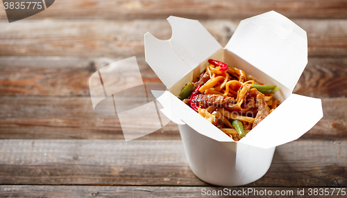 Image of Noodles with pork and vegetables in take-out box on wooden table