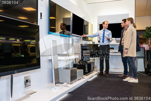 Image of Salesman Showing Flat Screen Tv To Couple In Store