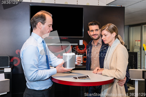 Image of Assistant Showing Compact Speaker To Couple In Shop