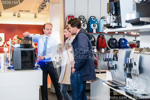 Image of Salesman Showing Coffee Maker To Couple In Store