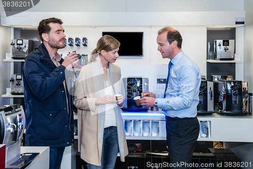 Image of Salesman Showing Espresso Cups To Couple In Electronic Shop