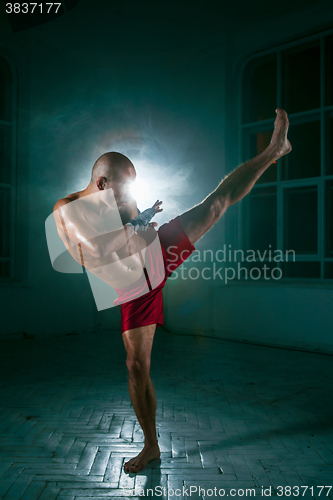 Image of The young man kickboxing in blue smoke