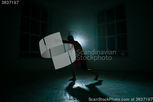 Image of The young man kickboxing on black background