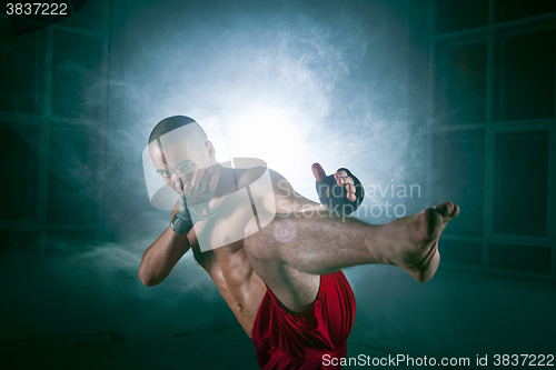 Image of The young man kickboxing in blue smoke