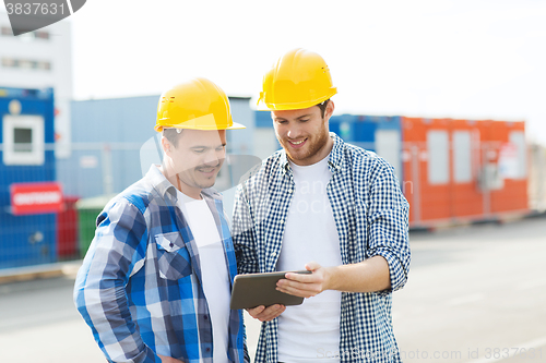 Image of two smiling builders in hardhats with tablet pc