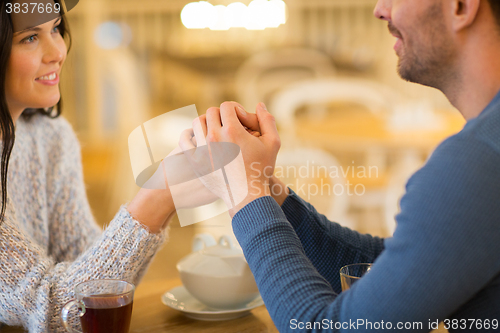 Image of happy couple with tea holding hands at restaurant