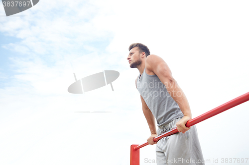 Image of young man exercising on horizontal bar outdoors