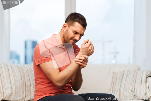 Image of unhappy man suffering from pain in hand at home