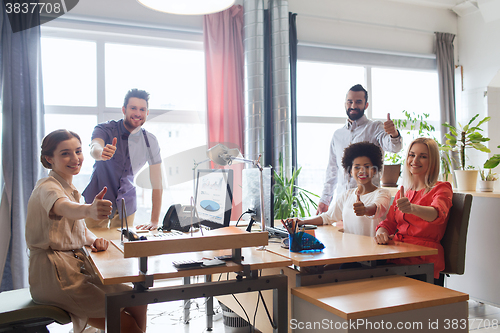 Image of happy creative team showing thumbs up in office