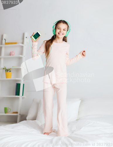 Image of girl jumping on bed with smartphone and headphones