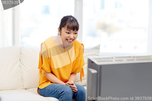 Image of happy asian young woman watching tv at home