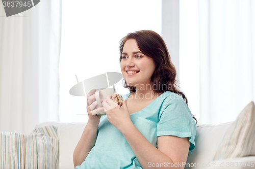 Image of happy plus size woman with cup and cookie at home