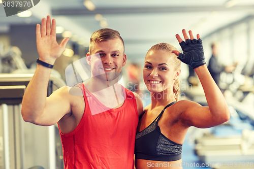 Image of smiling man and woman waving hands in gym