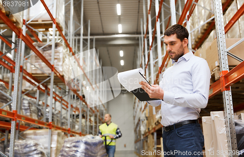 Image of businessman writing to clipboard at warehouse