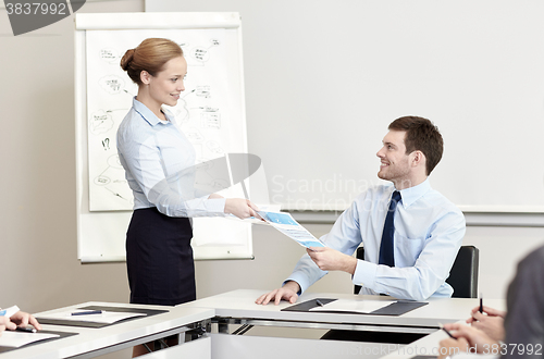 Image of smiling woman giving papers to man in office