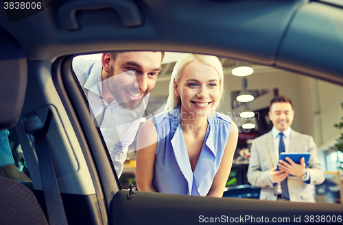 Image of happy couple with car dealer in auto show or salon