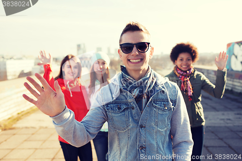 Image of happy teenage friends waving hands on city street