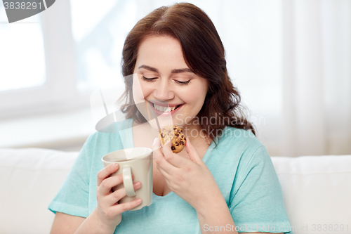 Image of happy plus size woman with cup and cookie at home