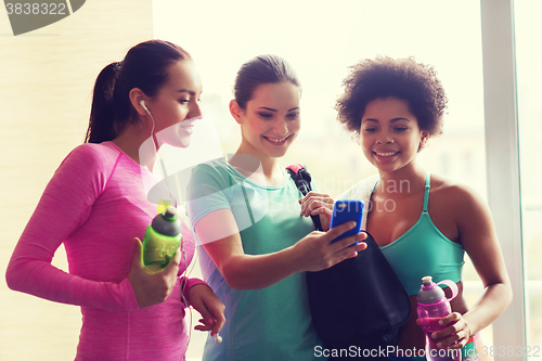 Image of happy women with bottles and smartphone in gym