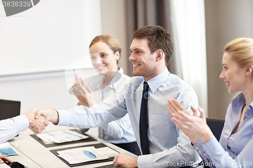 Image of smiling business team shaking hands in office