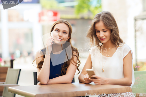 Image of happy young women with smartphones at outdoor cafe