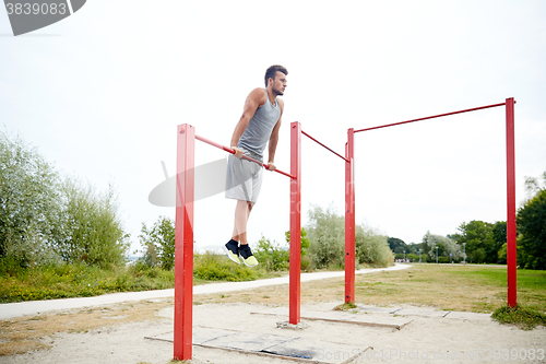 Image of young man exercising on horizontal bar outdoors