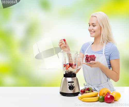 Image of smiling woman with blender preparing shake at home