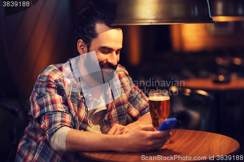 Image of man with smartphone and beer texting at bar