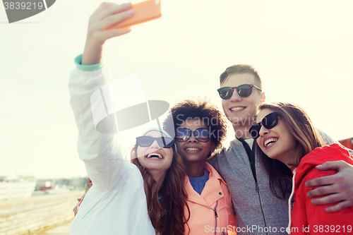 Image of smiling friends taking selfie with smartphone