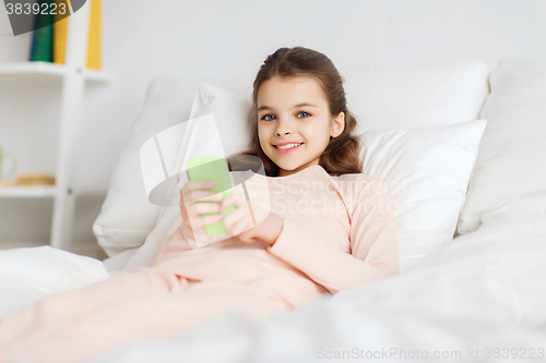 Image of happy girl lying in bed with smartphone at home