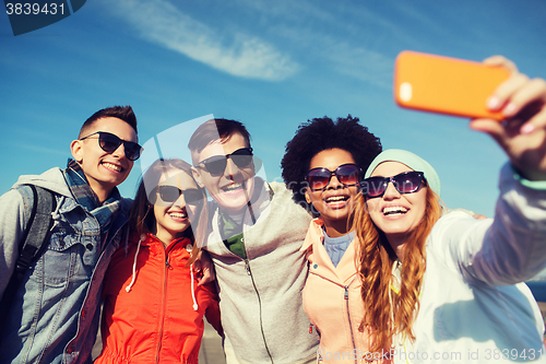 Image of smiling friends taking selfie with smartphone