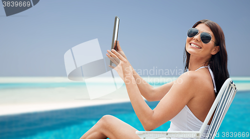 Image of smiling woman with tablet pc sunbathing on beach