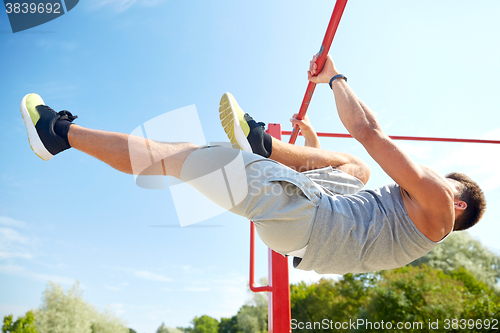 Image of young man exercising on horizontal bar outdoors