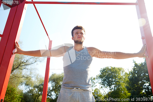 Image of young man exercising on horizontal bar outdoors