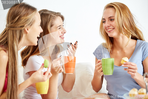 Image of happy young women drinking tea with sweets at home