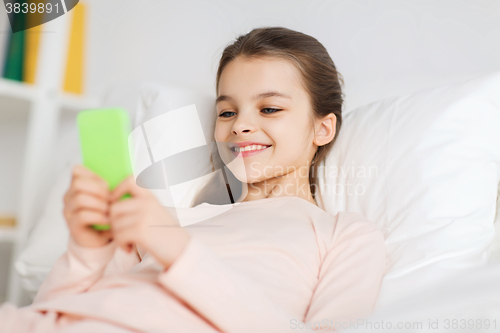 Image of happy girl lying in bed with smartphone at home