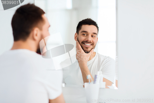 Image of happy young man looking to mirror at home bathroom