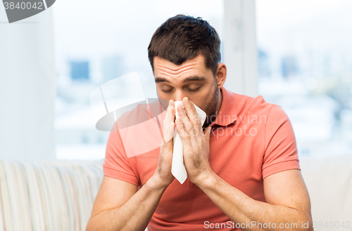 Image of sick man blowing nose to paper napkin at home
