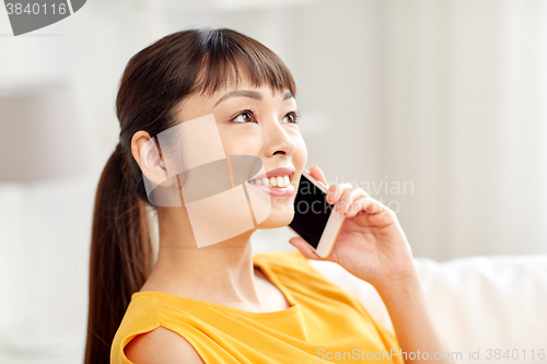 Image of happy asian woman calling on smartphone at home